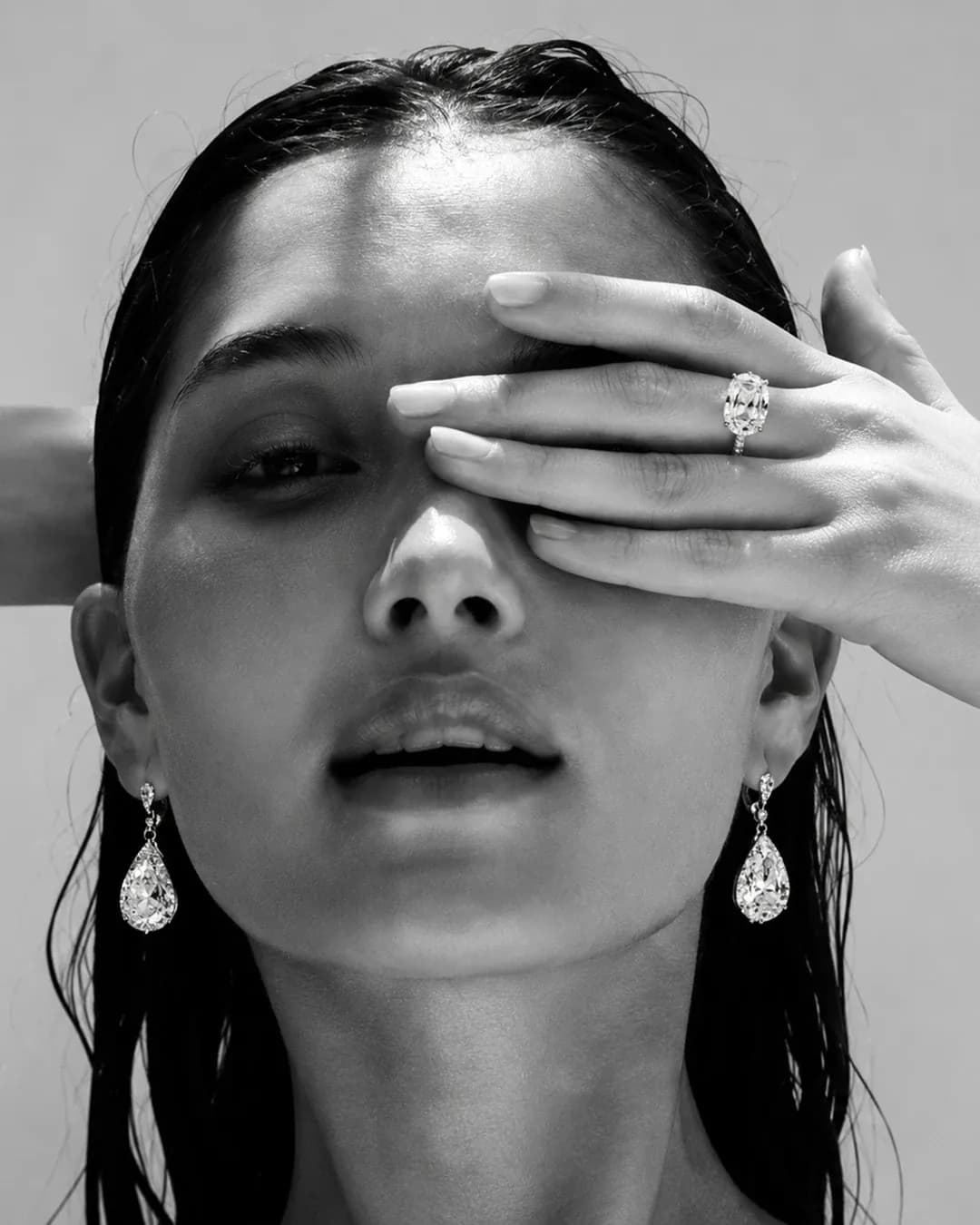 Model wearing Venori pear-cut diamond drop earrings and an oval diamond ring, black and white editorial